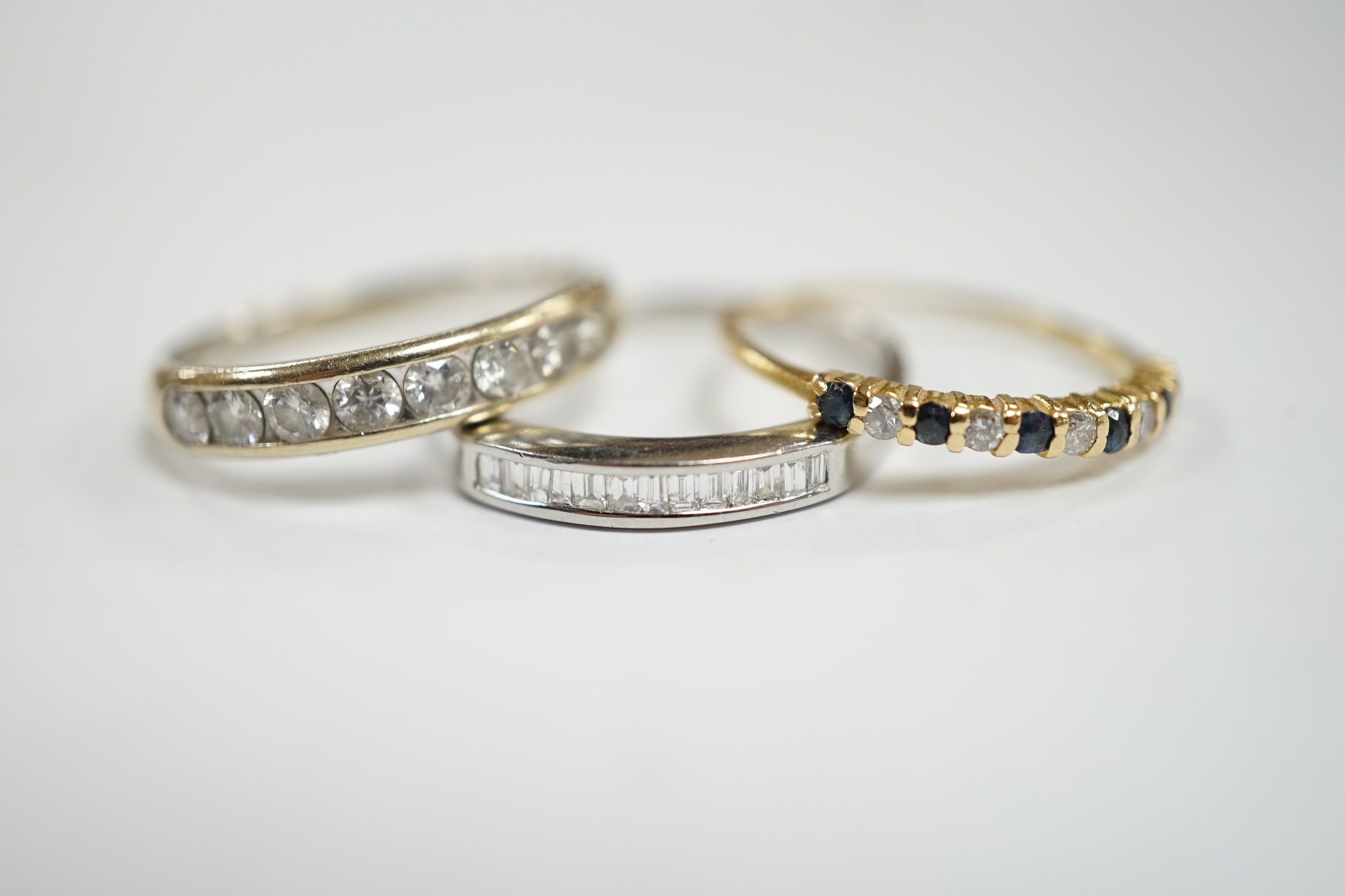 A white metal (stamped 950) and thirteen stone channel set baguette cut diamond ring, size O, together with two other unmarked gem set rings including diamond half eternity ring.